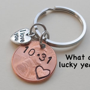 May include: A silver key chain with a copper penny charm. The penny has the year 10 31 2015 engraved on it. The charm also has a small silver heart with the words "I love you" engraved on it.