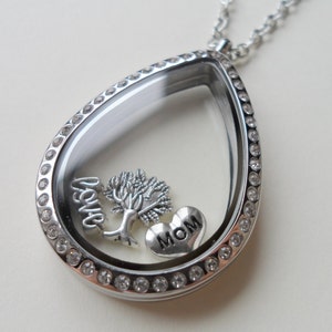 May include: Silver teardrop-shaped locket necklace with a clear glass insert. The locket contains a small silver tree charm, a silver charm with the word "love" and a silver heart charm with the word "MOM". The locket is surrounded by a row of clear rhinestones.