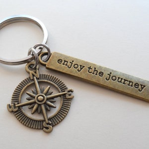 Pode incluir: Um amuleto de b&uacute;ssola de bronze com um chaveiro de prata e uma etiqueta de bronze que diz "enjoy the journey".