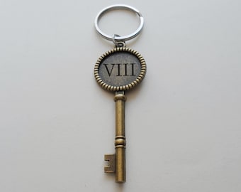 May include: Antique-style key with a silver keyring. The key is bronze-colored with a circular head featuring the Roman numeral VIII. The key's design includes a detailed, textured border around the numeral.