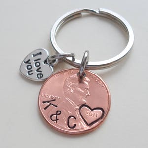 May include: A copper penny keychain with a heart engraved with the year 2011. The keychain also includes a silver heart charm with the words "I love you" engraved on it.