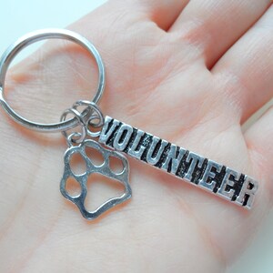 May include: Silver key chain with a paw print charm and a tag that says "Volunteer".