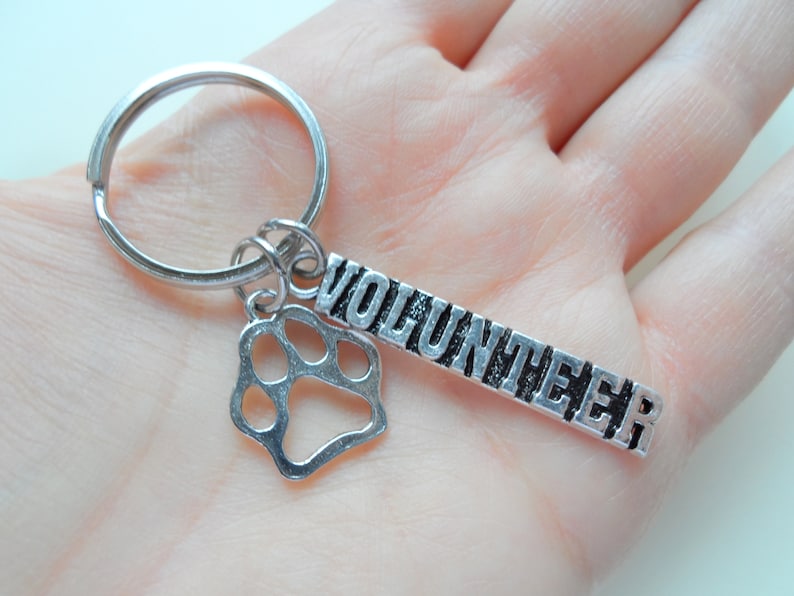 May include: Silver key chain with a paw print charm and a tag that says "Volunteer".