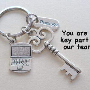 May include: A silver-toned metal keychain featuring a circular ring, a laptop charm, a decorative skeleton key charm, and a rectangular tag engraved with the text Thank you. The image includes the text You are a key part of our team!