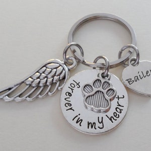May include: Silver keychain with a paw print charm, angel wing charm, and a heart charm with the name "Bailey" engraved on it. The charm with the paw print says "forever in my heart".