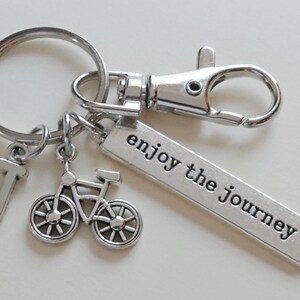 Pu&ograve; includere: Portachiavi color argento con un ciondolo a forma di bicicletta, un ciondolo con la lettera "J" e un'etichetta rettangolare con la scritta "enjoy the journey". Il portachiavi include un moschettone e un portachiavi.
