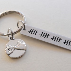 May include: Silver keychain with a rectangular tag marked with tally marks, indicating a count. A round charm with clasped hands hangs below the tag. The keychain is made of metal and has a bright, reflective finish.