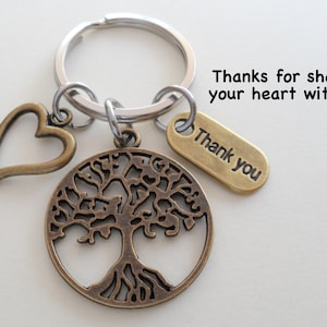 May include: A silver key chain with a bronze tree of life charm, a heart charm, and a tag that says "Thank you". The text "Thanks for sharing your heart with us!" is written above the keychain.