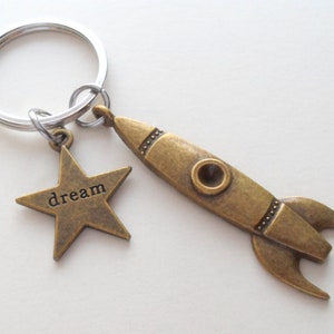 May include: A gold-toned rocket ship keychain with a star charm that says "dream".