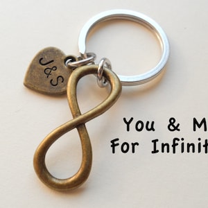 May include: A silver key chain with a bronze infinity symbol charm and a heart charm with the initials "J&S" engraved on it. The text "You & Me For Infinity!" is written below the charm.