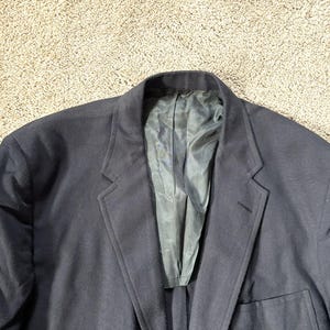 May include: A dark blue blazer made from a smooth, textured fabric. The blazer features a single-breasted closure and a notched lapel.