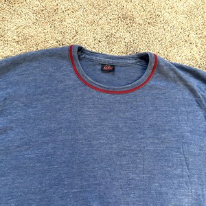 May include: A blue t-shirt with a red trim around the neckline. The shirt is made of a soft material and has short sleeves. The shirt is a solid color and appears to be pre-worn.
