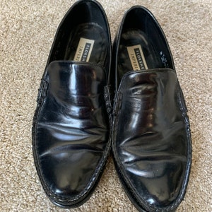 May include: A pair of black leather Florsheim Imperial loafers. The loafers have a stitched edge and a pointed toe.