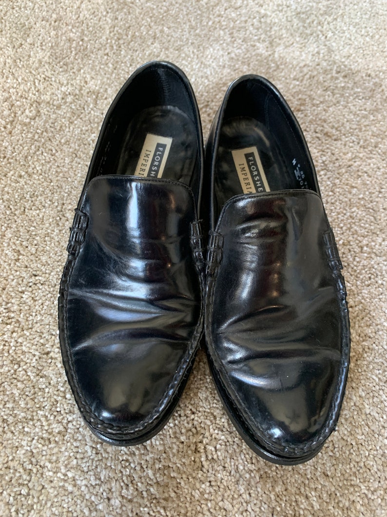 May include: A pair of black leather Florsheim Imperial loafers. The loafers have a stitched edge and a pointed toe.