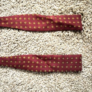 May include: Two burgundy bow ties with a gold and white geometric pattern.