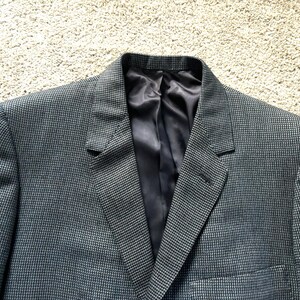 May include: A dark gray blazer with a subtle houndstooth pattern. The blazer has a notch lapel and a single button closure.