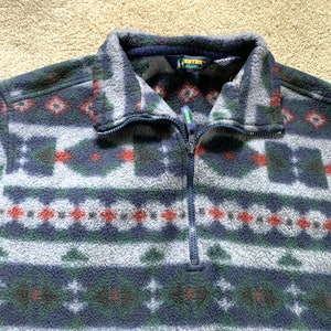 May include: A blue, green, red, and white patterned fleece pullover with a half-zip closure. The zipper has a green pull tab. The brand name "Eddie Bauer" is visible on the tag.