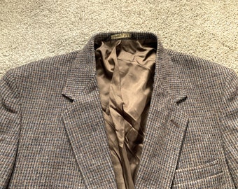 May include: A brown and blue tweed blazer with a notched lapel and a brown satin lining. The jacket has a classic, tailored fit and a two-button closure. The blazer is a vintage style.