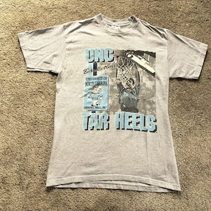 May include: Gray t-shirt with a blue and white graphic print of a basketball player dunking. The graphic includes the text "UNC Basketball, University of North Carolina, Chapel Hill, NC, Tar Heels".