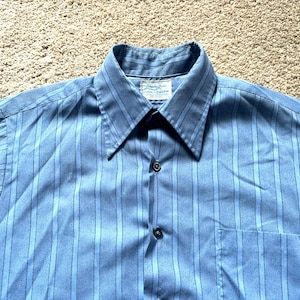 May include: A blue striped long-sleeved shirt with a button-down collar and a single button pocket on the left side. The shirt has a white label with the text "London Fog" on it.