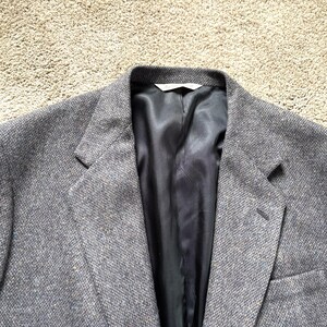 Puede incluir: Blazer de tweed gris con solapas de muesca y diseño de un solo pecho. El blazer tiene un forro negro y un bolsillo en el pecho. La tela tiene un sutil estampado moteado. Un estilo clásico.