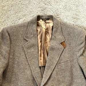 May include: A brown and white checkered blazer with a brown label on the right side of the chest. The blazer has a single button closure and a pocket on the left side.