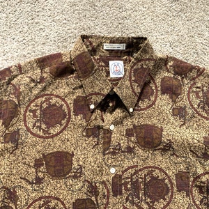 May include: A brown and tan button-down shirt with a repeating pattern of brown and red circles with a design inside. The shirt has a white collar and a white button-down closure. The shirt has a small white tag with the text "The Original" and a logo of an anchor with a red, white, and blue design.