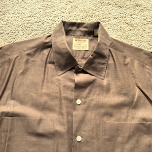 May include: A brown long-sleeve button-down shirt with a collar and two pockets. The shirt has a label that reads "Wrangler" and "100% Cotton".
