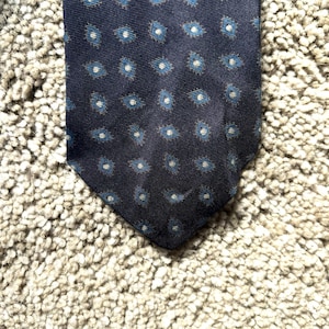 May include: A dark blue silk tie with a white and blue geometric pattern.