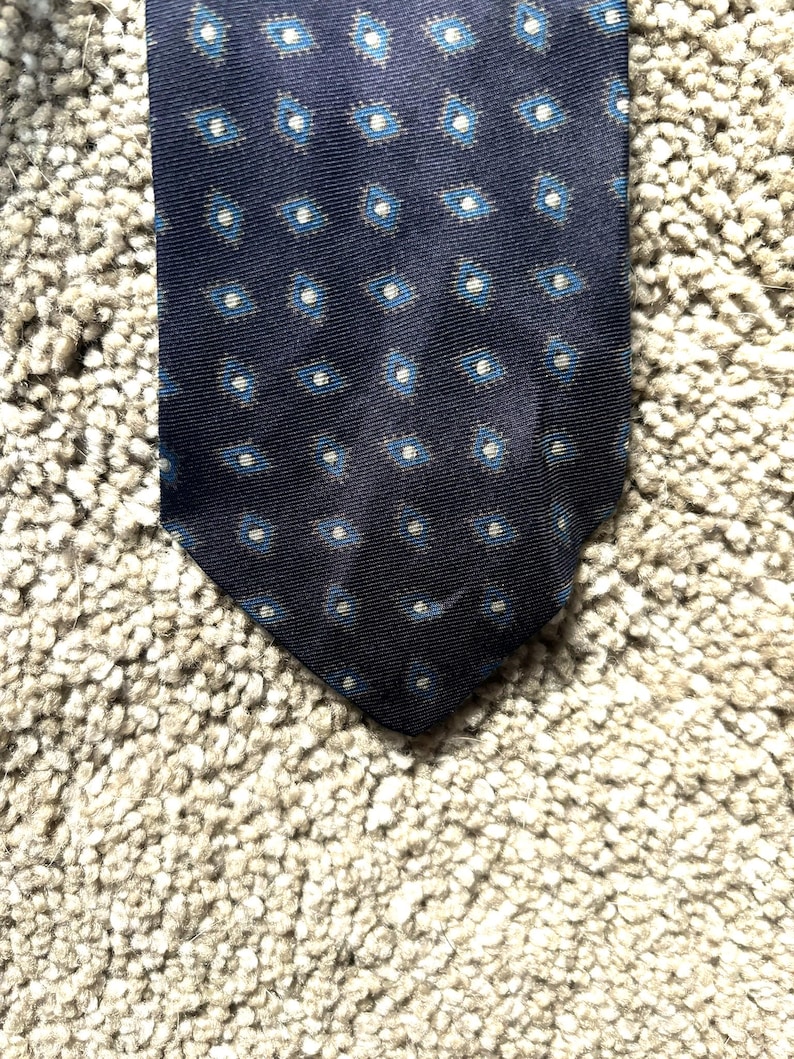 May include: A dark blue silk tie with a white and blue geometric pattern.