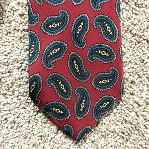 Puede incluir: Una corbata roja con estampado de paisley con un diseño de paisley azul oscuro y verde.
