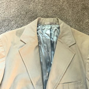 May include: A beige blazer with a blue satin lining. The blazer has a single button closure and a pocket on the left side.