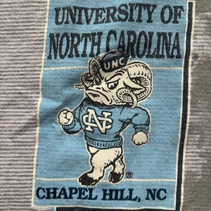 May include: A vintage t-shirt featuring a blue and white mascot with the text "University of North Carolina, Chapel Hill, NC".