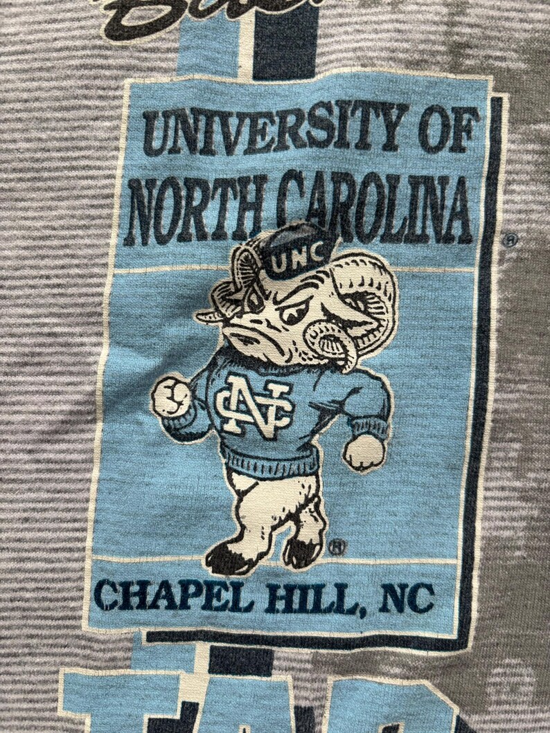 May include: A vintage t-shirt featuring a blue and white mascot with the text "University of North Carolina, Chapel Hill, NC".