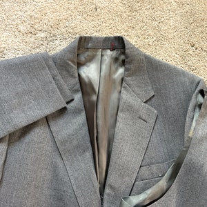 May include: A gray blazer with a black satin lining. The blazer has a single button closure and a pocket on the left side.