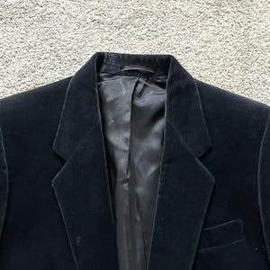 Peut inclure: Un blazer en velours noir avec un col cranté et une fermeture à un bouton. Le blazer a une texture lisse et luxueuse.