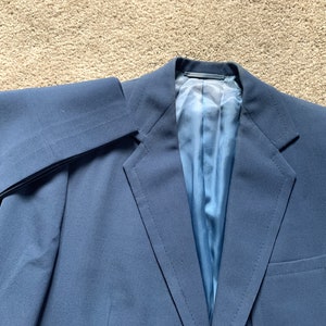 May include: A dark blue blazer with a single button closure and a pocket on the right side. The blazer is made of a smooth, wrinkle-resistant fabric.