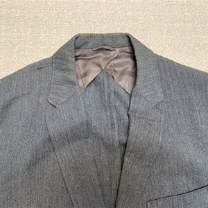 Puede incluir: Una chaqueta gris de rayas finas con forro de satén. La chaqueta tiene un cuello de muesca y un cierre de un botón.