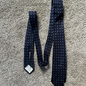 May include: A dark blue tie with a white and blue patterned design. The tie has a label that reads "Barneys New York".