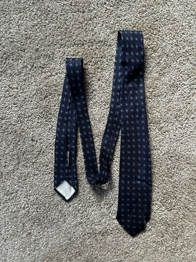 May include: A dark blue tie with a white and blue patterned design. The tie has a label that reads "Barneys New York".