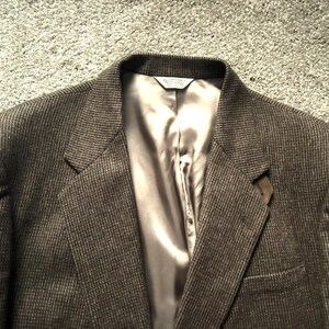 May include: A brown tweed blazer with a notched lapel and a satin lining. The jacket has a two-button closure and a single chest pocket. The fabric has a subtle pattern, and the blazer appears to be in good condition.