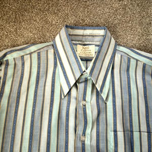 May include: A striped long-sleeve shirt with a button-down collar. The shirt has blue, green, and yellow stripes. The label reads "Kent Collection by Arrow, The New Wrinkle",