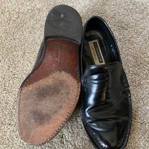May include: A pair of black leather Florsheim Imperial loafers with a pointed toe. The loafers have a leather sole and a gold embossed logo on the side.