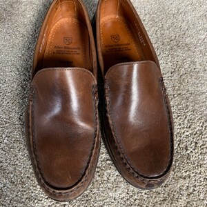 May include: A pair of brown leather loafers with a stitched seam around the edge. The loafers have a leather insole with the Allen Edmonds logo and the text "Handcrafted in USA of fine imported leather".