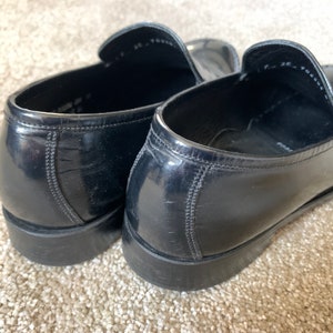 May include: A pair of black leather loafers with a shiny finish. The loafers have a pointed toe and a low heel.