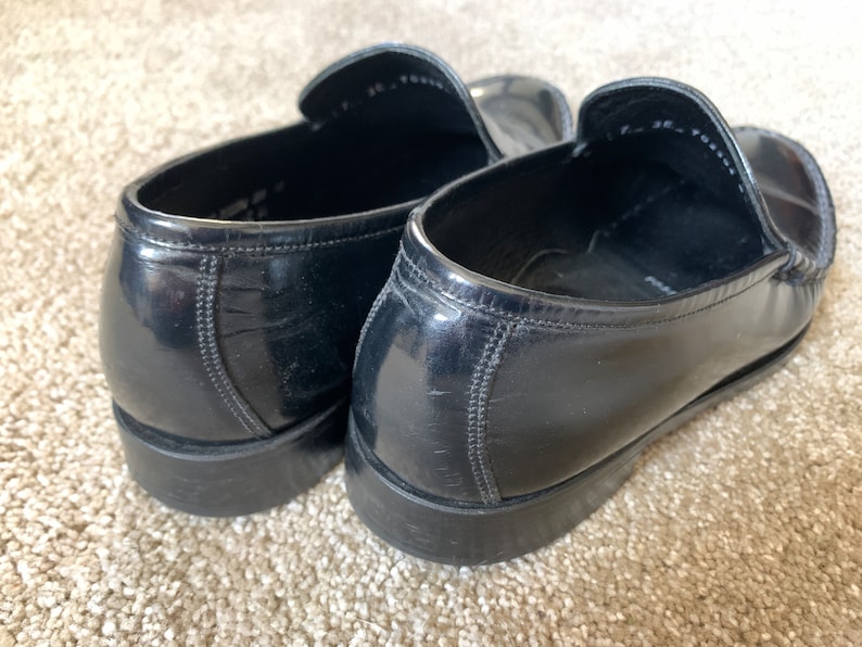 May include: A pair of black leather loafers with a shiny finish. The loafers have a pointed toe and a low heel.