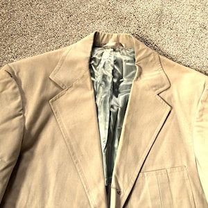 May include: A beige blazer with a single button closure and a pocket on the right side. The blazer is made of a soft, textured fabric.