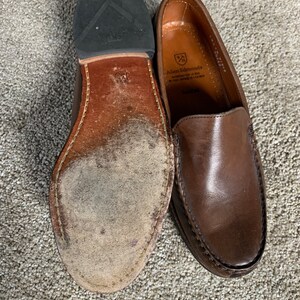 May include: A pair of brown leather loafers with a black rubber sole. The loafers have a leather lining and a leather insole. The brand name "Allen Edmonds" is printed on the insole.