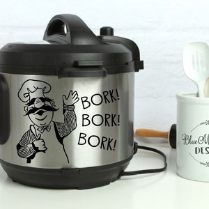 May include: A black and silver electric pressure cooker with a cartoon chef sticker on the front. The sticker says "Bork! Bork! Bork!"