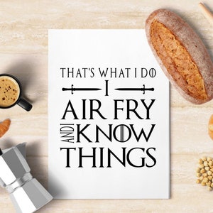 May include: White kitchen towel with black text that reads "That's what I do, I air fry and I know things". The text is in a font similar to the Game of Thrones logo.